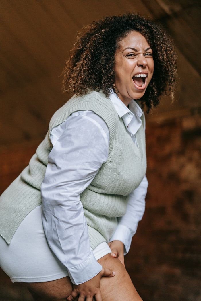 ÜROJİNEKOLOJİ Energetic woman with curly hair in a vest and shirt expressing emotion indoors.