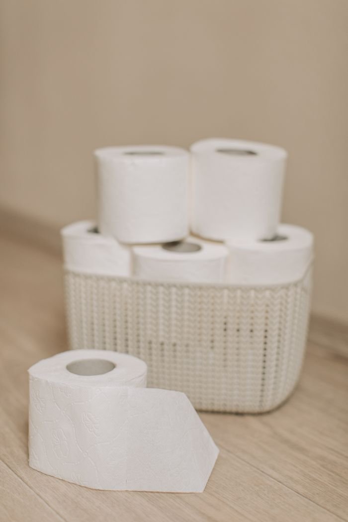 ÜROJİNEKOLOJİ Collection of toilet paper rolls neatly arranged in a woven basket on a wooden floor, indicating hygiene and cleanliness.