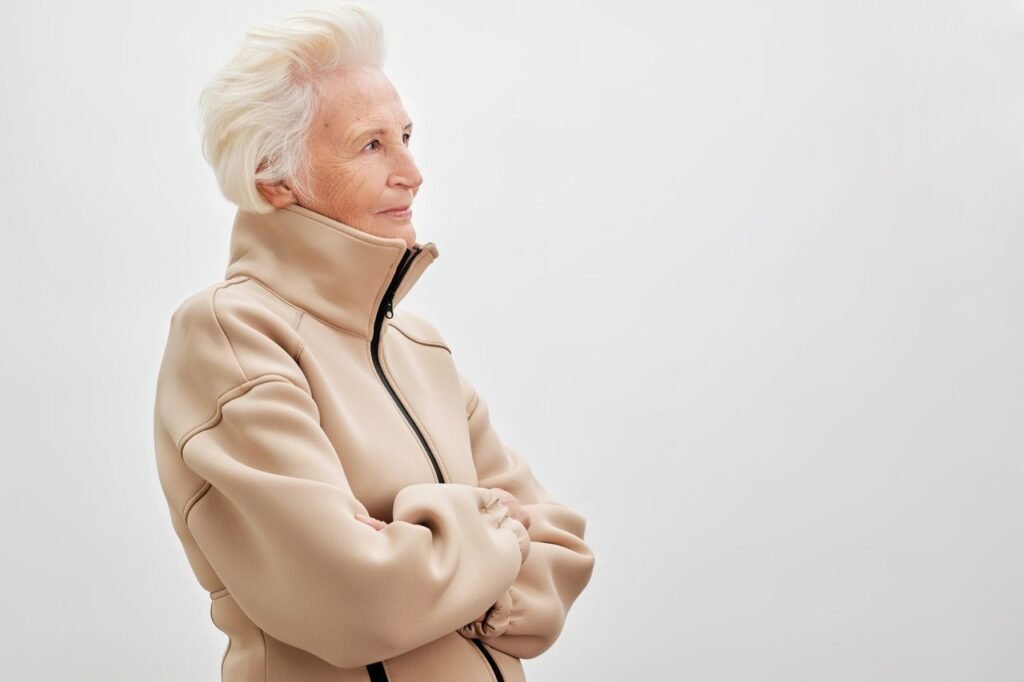 Side view of elderly woman with white hair in a beige jacket against a neutral background.