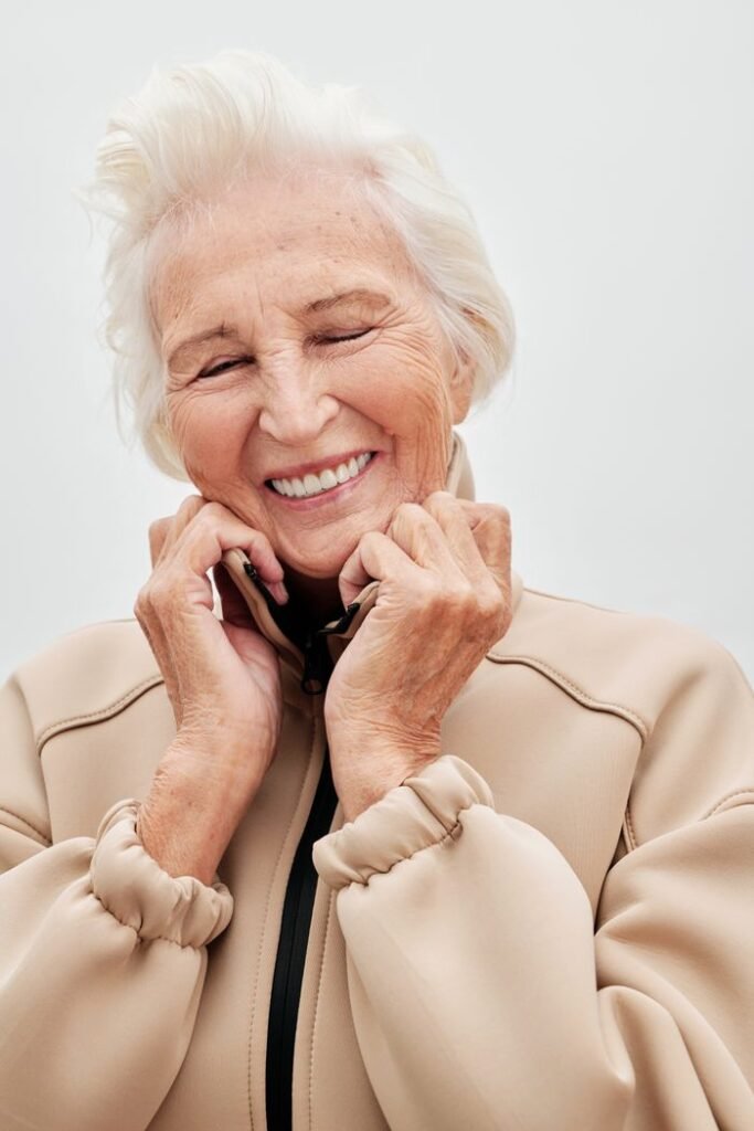 Happy senior woman in beige jacket smiling with eyes closed, enjoying a light moment.