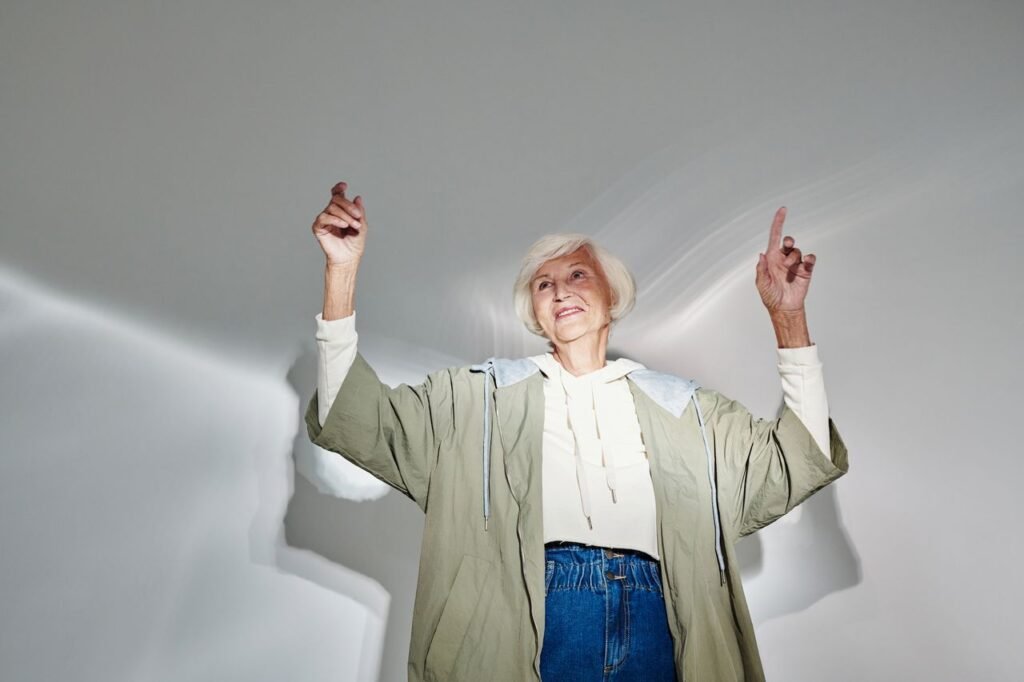 Fashionable elderly woman raising arms in stylish outfit with white hair and denim jeans.