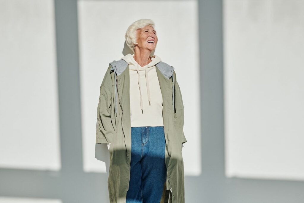Senior woman smiling while wearing a chic coat and jeans, embracing modern fashion with a joyful expression.