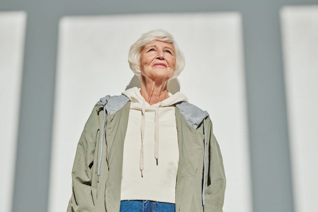 Portrait of a stylish senior woman in a coat and hoodie, embracing modern fashion outdoors.