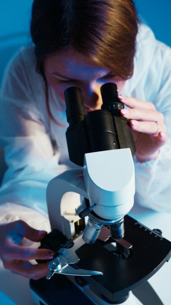 A female scientist wearing protective gear analyzing a sample using a microscope in a laboratory.