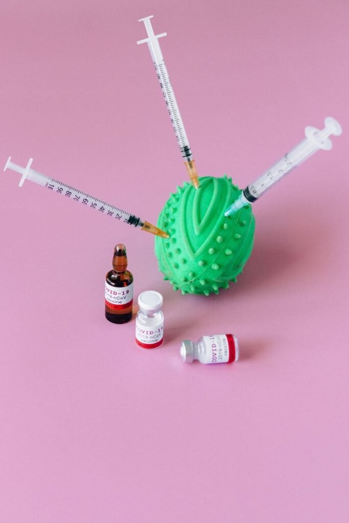 Syringes and medical vials arranged on a pink background with stress ball.